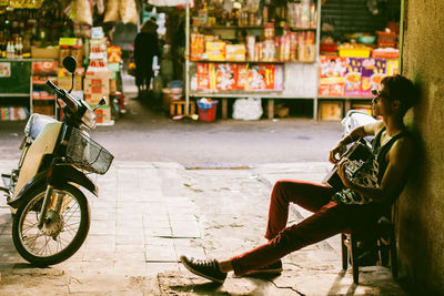 Man playing guitar while sitting on footpath at market