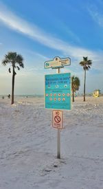 Information sign on beach against blue sky