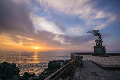 Statue by sea against sky during sunset