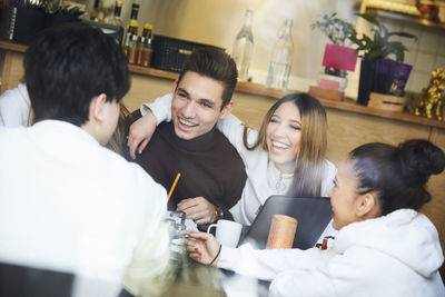 Male and female friends smiling while sitting at table in cafe