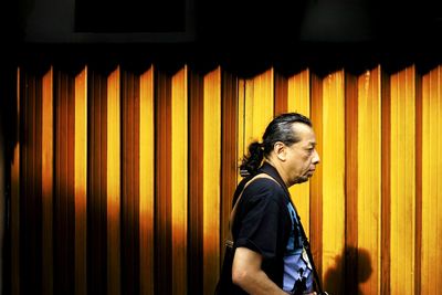 Side view of young woman standing against illuminated wall