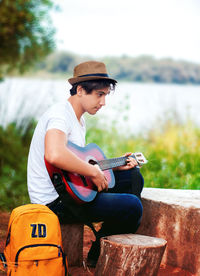 Side view of young man playing guitar while sitting outdoors