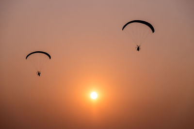 Low angle view of silhouette people paragliding against clear sky during sunset