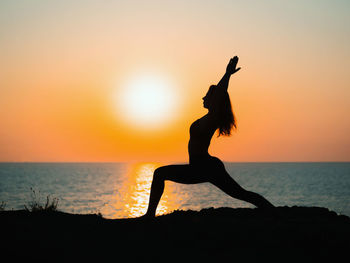 Silhouette woman doing yoga at beach against sky during sunset