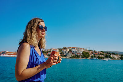 Woman taking photo with instant camera near sea and coastal town