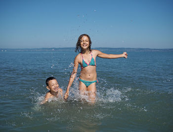 Siblings wading in sea against clear sky