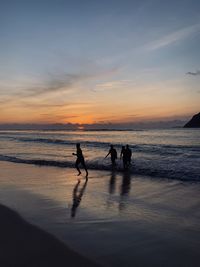 Silhouette people on beach against sky during sunset