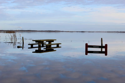 Bench on lake against sky