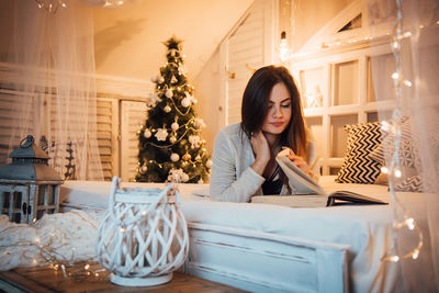 Woman reading book while lying on bed at home during christmas