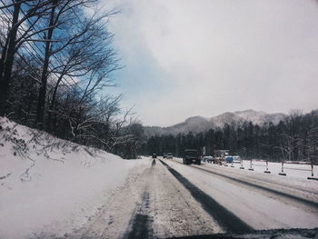 Road by bare trees against sky during winter