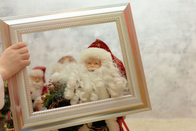 Cropped hands holding frame by santa claus figurine