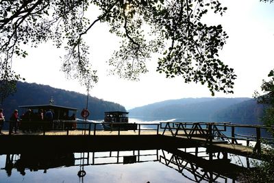 People on bridge over lake against sky