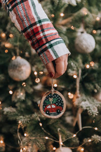 Female hand holding diy wooden handcrafted christmas ornament in front of christmas tree