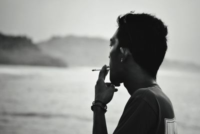 Side view of man smoking cigarette at beach against sky