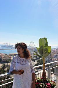 Woman standing leaning on railing against sky