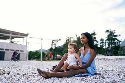 Happy girl sitting on woman against sky