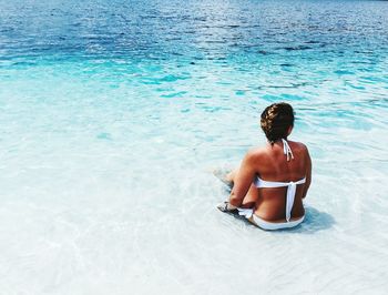 Rear view of mid adult woman sitting at beach