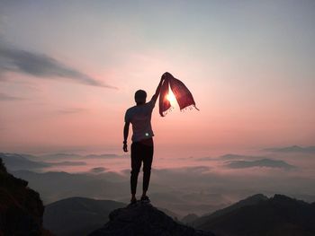 Rear view of man holding scarf on mountain against sky during sunset