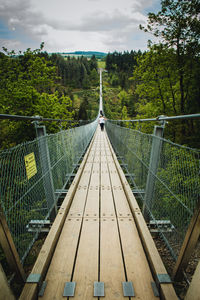 Footbridge in forest against sky
