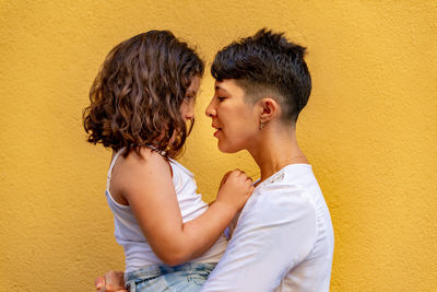 Side view of couple kissing against yellow wall