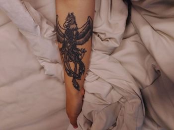 Cropped hand of woman with tattoo on bed