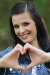 Portrait of smiling young woman making heart shape against trees