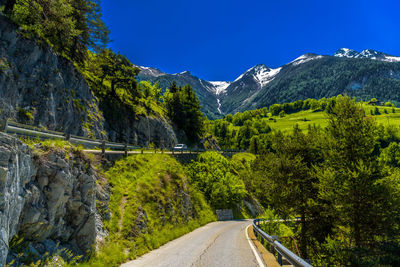 Road amidst trees and mountains against blue sky