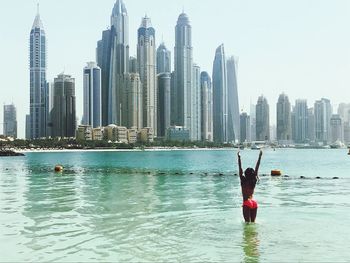 Young woman enjoying in sea against buildings