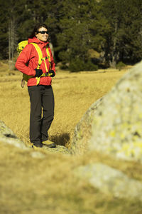 Smiling hiker standing amidst rocks on field against forest