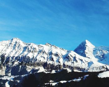 Low angle view of snowcapped mountains against clear blue sky