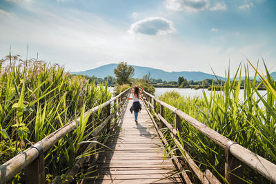 Rear view of woman walking amidst plants against sky