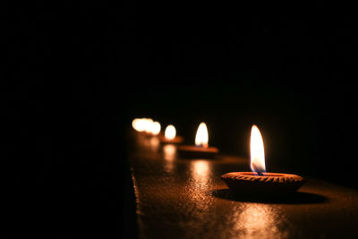 Close-up of lit diyas on retaining wall against black background