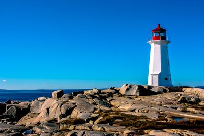 Lighthouse on rock by sea against clear blue sky