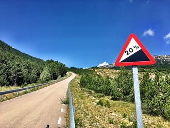 Road sign by trees against blue sky