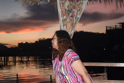 Portrait of woman standing by lake against sky during sunset