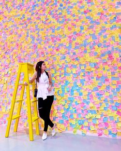 Full length of woman standing against multi colored adhesive notes on wall