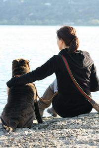 Rear view of woman sitting with dog on rock formation while looking at river