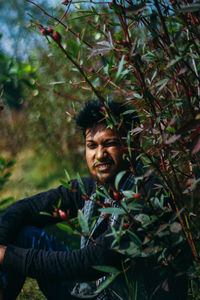 Portrait of young man sitting by plants in forest