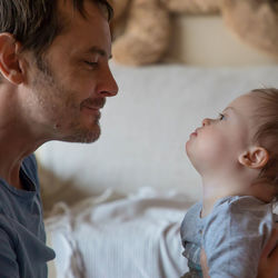 Close-up of father with son sitting on bed at home