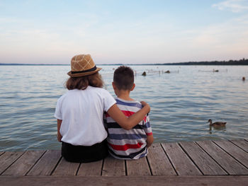 Rear view of people sitting on shore against sky