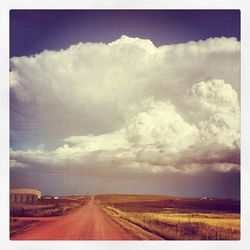 Road passing through field against cloudy sky