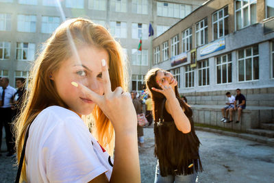 Portrait of smiling young friends showing peace sign on street