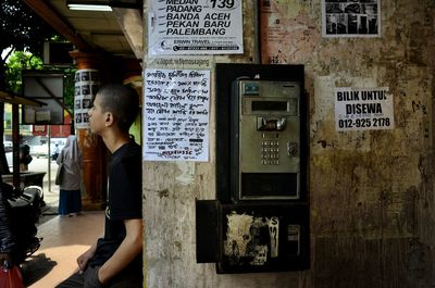 Side view of boy leaning on wall by pay phone