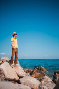 Rear view of man standing on rock at beach against clear blue sky