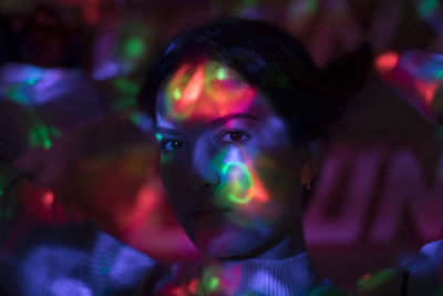 Close-up portrait of woman with colorful lights on face in nightclub