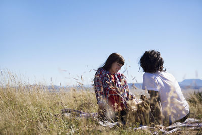 Couple sitting on field against clear sky