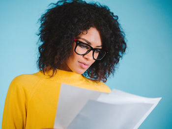 Young woman wearing eyeglasses reading documents against blue background