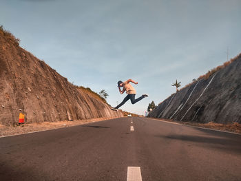 Man jumping on road against sky