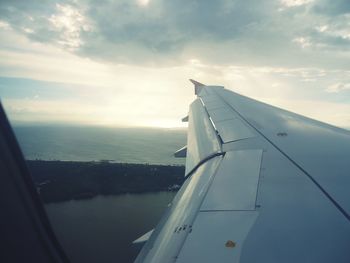 Airplane flying over sea against sky during sunset