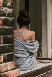 Young woman sitting in an open old window, back view. conceptual romantic, dreaming, hope, lonely.